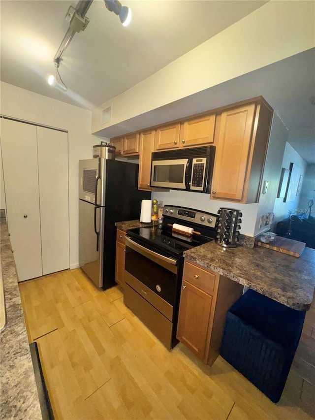 kitchen with rail lighting, kitchen peninsula, dark stone counters, light hardwood / wood-style floors, and appliances with stainless steel finishes