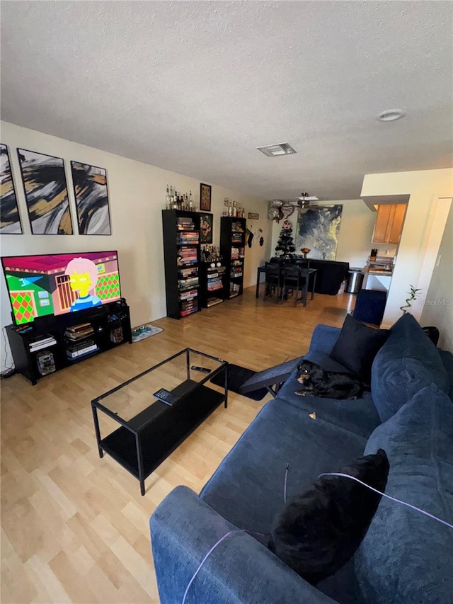 living room with ceiling fan, a textured ceiling, and hardwood / wood-style flooring