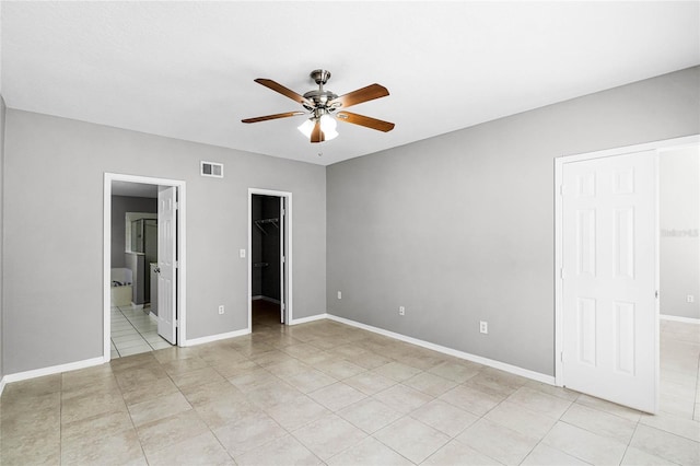 unfurnished bedroom with light tile patterned floors, a walk in closet, ensuite bathroom, and ceiling fan