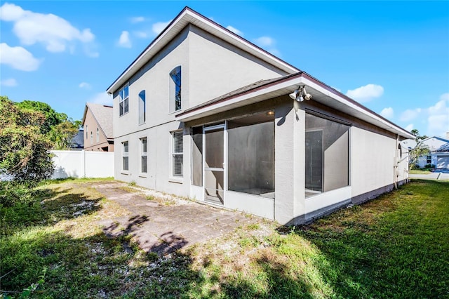 rear view of property featuring a lawn, a sunroom, and a patio area