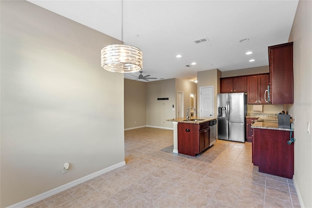 kitchen with stainless steel refrigerator with ice dispenser, light stone counters, sink, a center island with sink, and hanging light fixtures