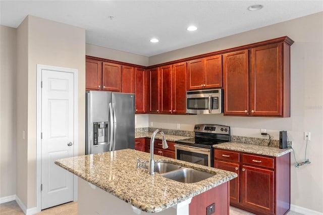 kitchen with light stone countertops, stainless steel appliances, a center island with sink, and sink