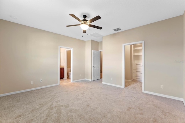 unfurnished bedroom with ensuite bath, a spacious closet, ceiling fan, light colored carpet, and a closet