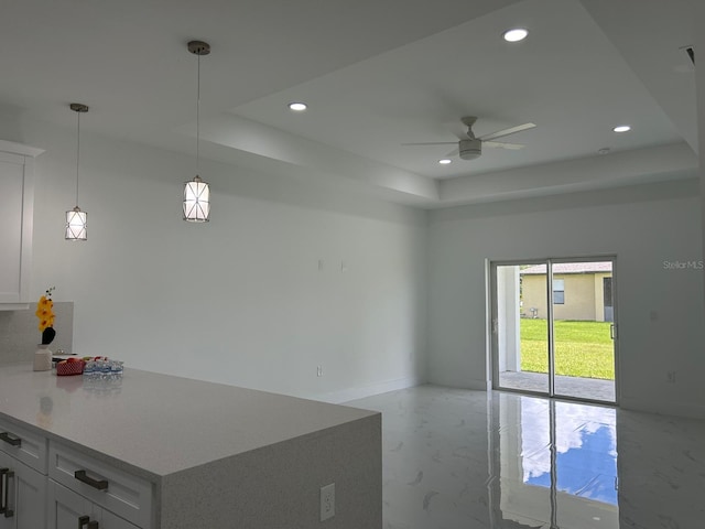 kitchen featuring white cabinetry, hanging light fixtures, a raised ceiling, and ceiling fan