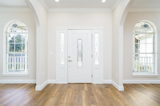 entryway with ornamental molding, a wealth of natural light, and light hardwood / wood-style flooring