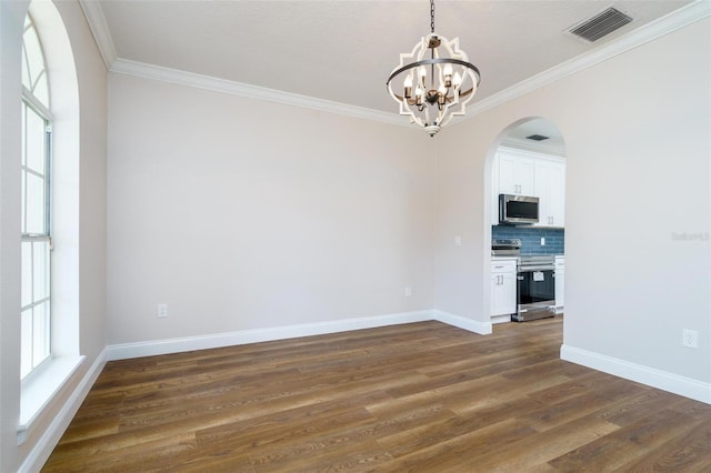 empty room with a healthy amount of sunlight, ornamental molding, dark wood-type flooring, and a chandelier