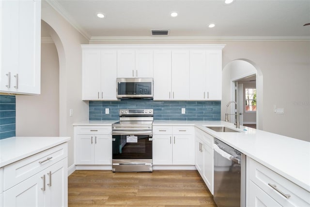 kitchen featuring light wood-type flooring, ornamental molding, stainless steel appliances, sink, and white cabinets