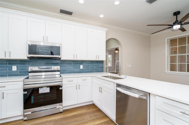 kitchen featuring appliances with stainless steel finishes, ornamental molding, sink, light hardwood / wood-style flooring, and white cabinets