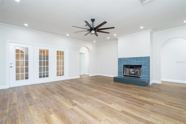 unfurnished living room with a tile fireplace, ceiling fan, crown molding, and light hardwood / wood-style floors