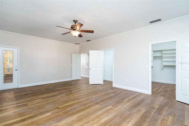 unfurnished bedroom with a walk in closet, ceiling fan, hardwood / wood-style floors, and ornamental molding