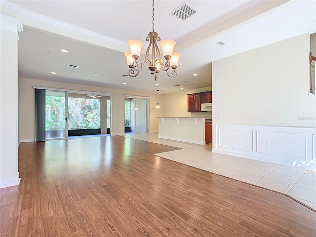 unfurnished living room with an inviting chandelier, light hardwood / wood-style flooring, and ornamental molding