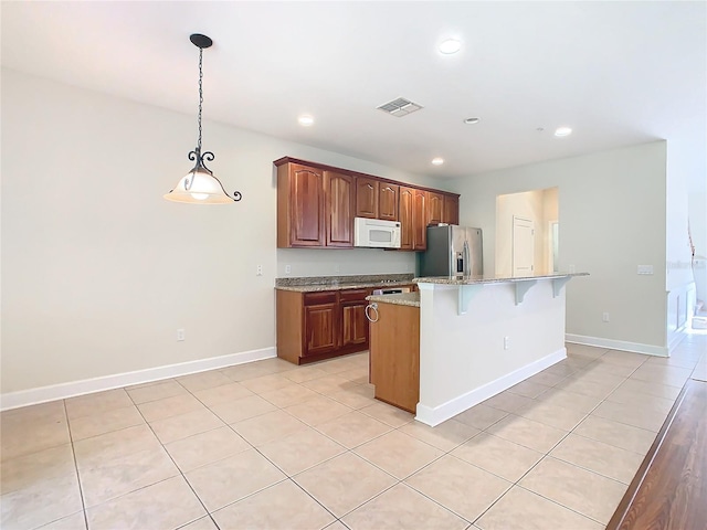 kitchen featuring a kitchen island with sink, hanging light fixtures, stainless steel refrigerator with ice dispenser, light tile patterned flooring, and light stone counters