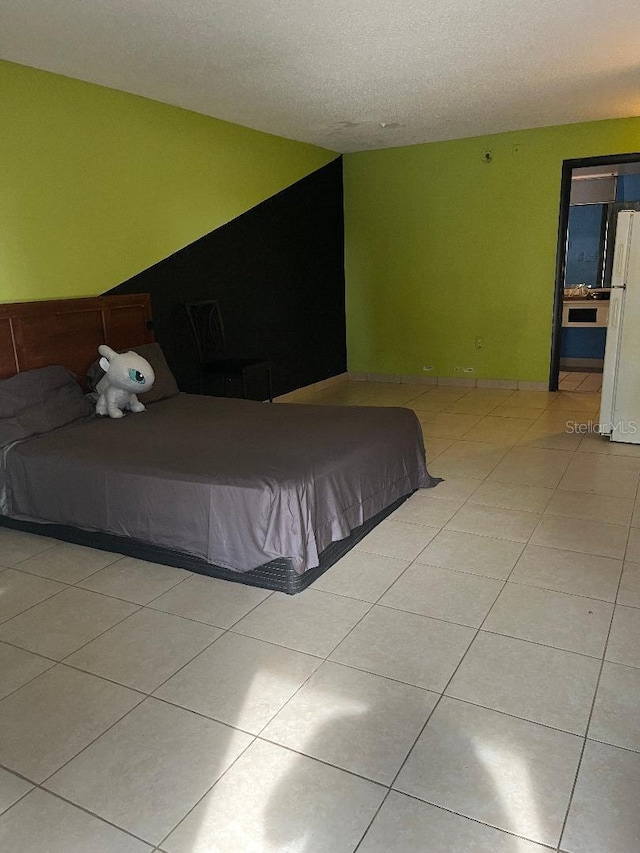 unfurnished bedroom with white refrigerator, light tile patterned floors, and a textured ceiling