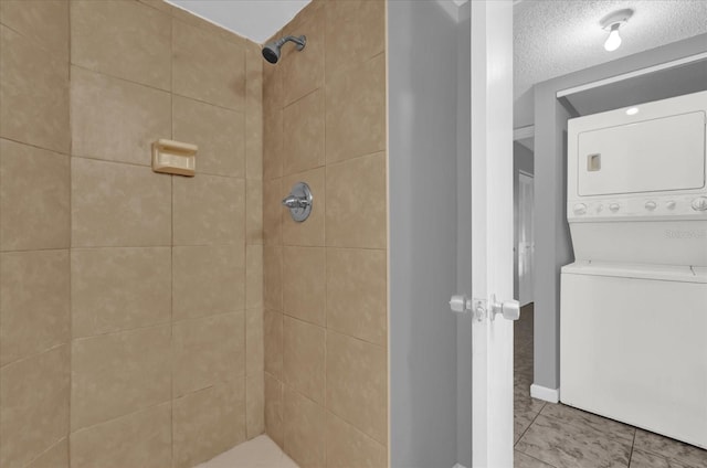 bathroom featuring a tile shower, tile patterned floors, stacked washer and dryer, and a textured ceiling