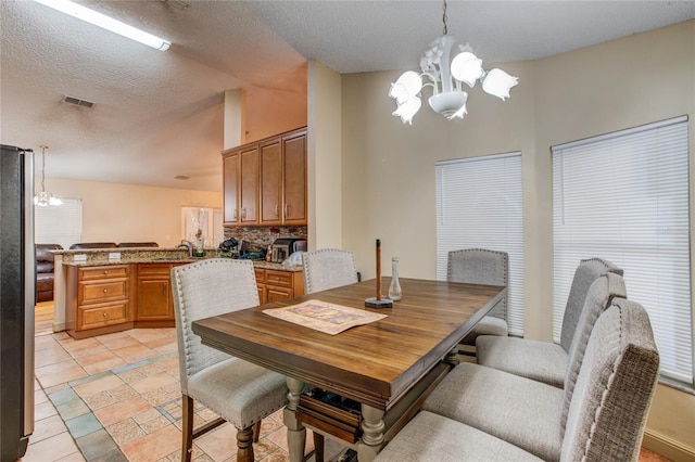 tiled dining area featuring sink, a textured ceiling, and an inviting chandelier