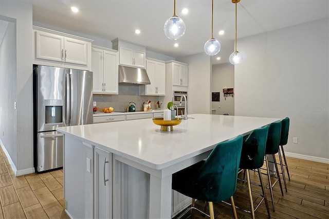 3359 Hanging Tide St, Winter Garden, FL 34787 - kitchen with stainless steel fridge with ice dispenser, under cabinet range hood, wood tiled floors, a large island, and white cabinetry
