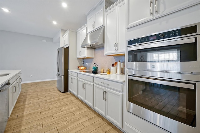 3359 Hanging Tide St, Winter Garden, FL 34787 - kitchen with stainless steel appliances, under cabinet range hood, white cabinetry, light wood-style floors, and tasteful backsplash