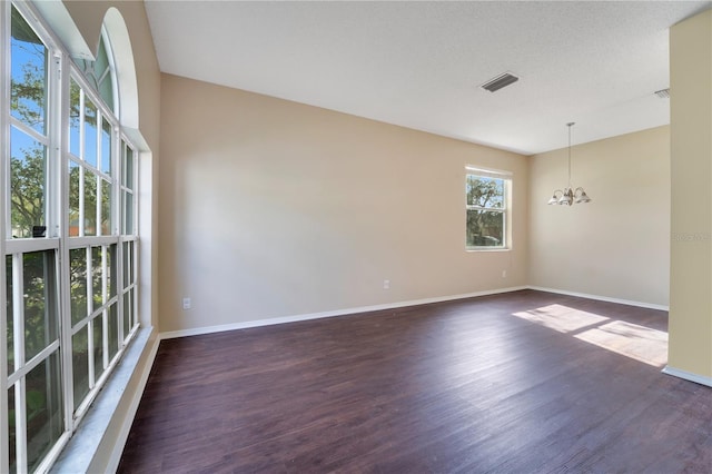 spare room with dark hardwood / wood-style flooring, a textured ceiling, and a notable chandelier