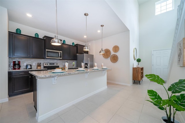 kitchen featuring light stone countertops, a breakfast bar, stainless steel appliances, decorative light fixtures, and a center island with sink