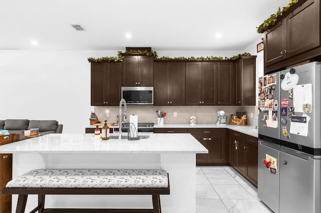 kitchen with a kitchen bar, a kitchen island with sink, and appliances with stainless steel finishes