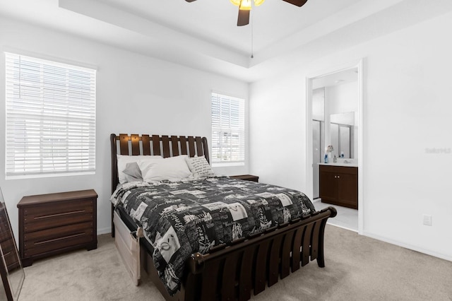 carpeted bedroom featuring baseboards, ensuite bath, a tray ceiling, and a ceiling fan