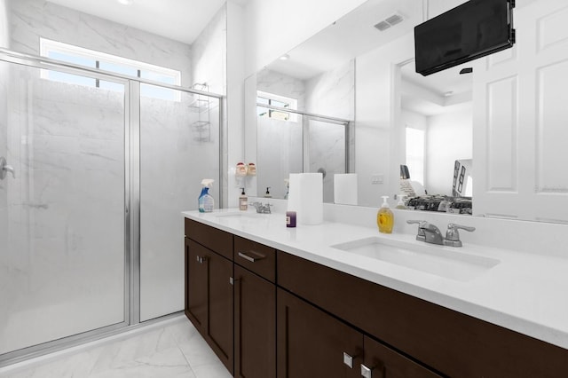 full bathroom with double vanity, marble finish floor, a marble finish shower, and a sink