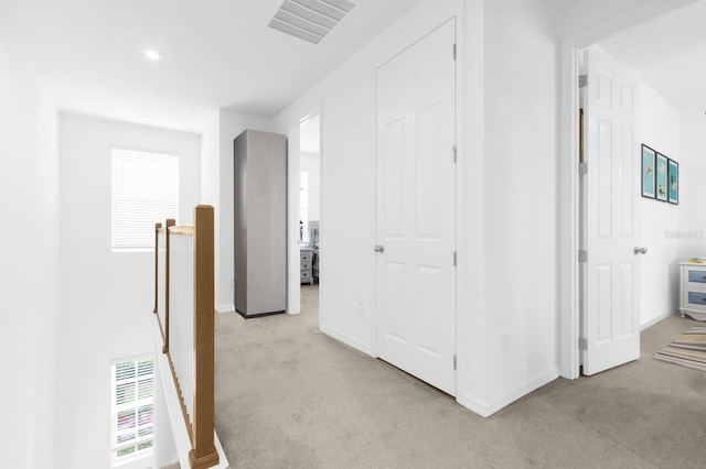 corridor with an upstairs landing, visible vents, and light colored carpet