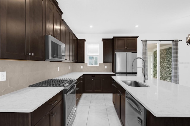 kitchen featuring dark brown cabinetry, a sink, appliances with stainless steel finishes, tasteful backsplash, and a center island with sink