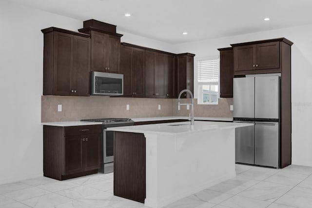 kitchen featuring stainless steel appliances, a sink, dark brown cabinets, light countertops, and an island with sink