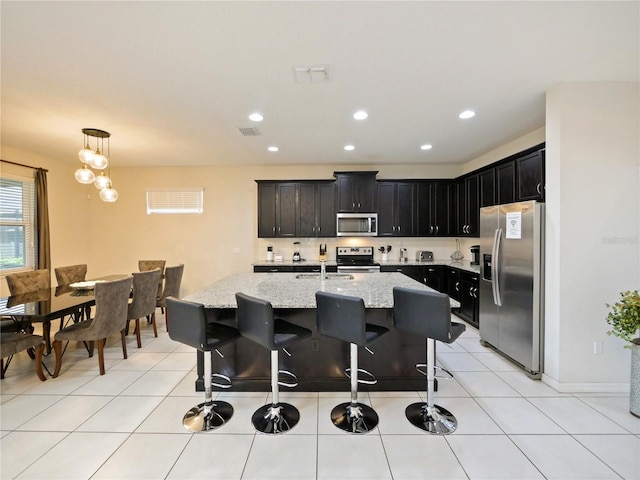 kitchen with light stone countertops, stainless steel appliances, a kitchen breakfast bar, decorative light fixtures, and a center island with sink