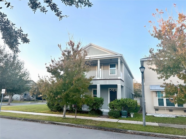 view of front facade with covered porch, a front yard, and a balcony