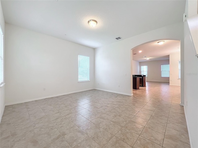 unfurnished room with arched walkways, a wealth of natural light, visible vents, and baseboards