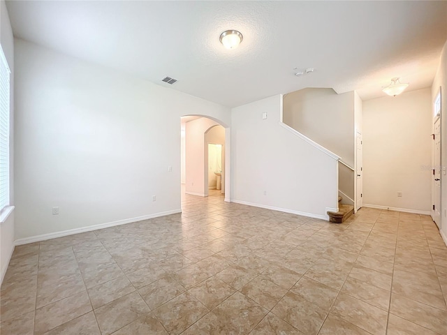 spare room featuring arched walkways, a textured ceiling, visible vents, baseboards, and stairway