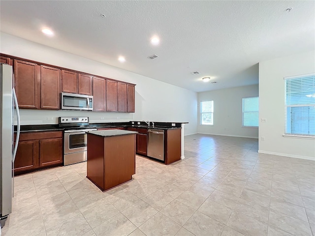 kitchen featuring dark countertops, visible vents, appliances with stainless steel finishes, open floor plan, and a kitchen island