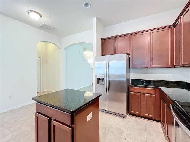 kitchen featuring a center island, stainless steel appliances, visible vents, a textured ceiling, and dark stone countertops