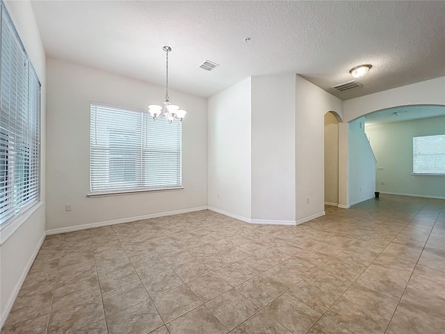 spare room with an inviting chandelier, baseboards, visible vents, and arched walkways