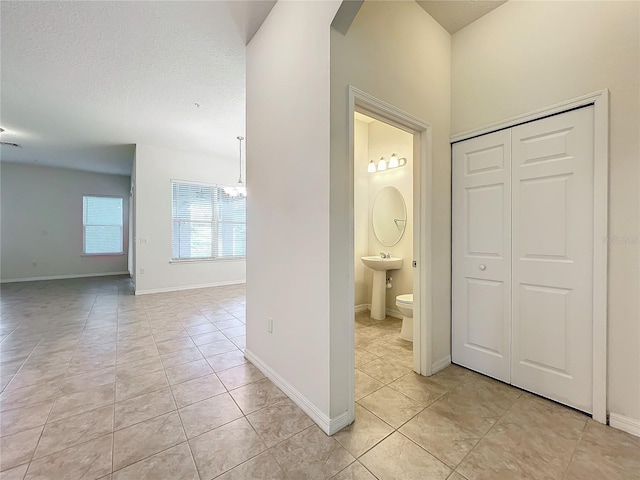 hall with a textured ceiling, light tile patterned flooring, arched walkways, and baseboards