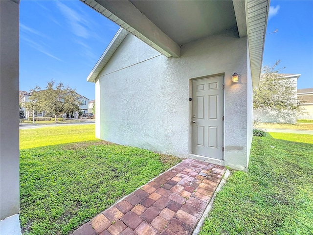 doorway to property featuring a lawn and stucco siding