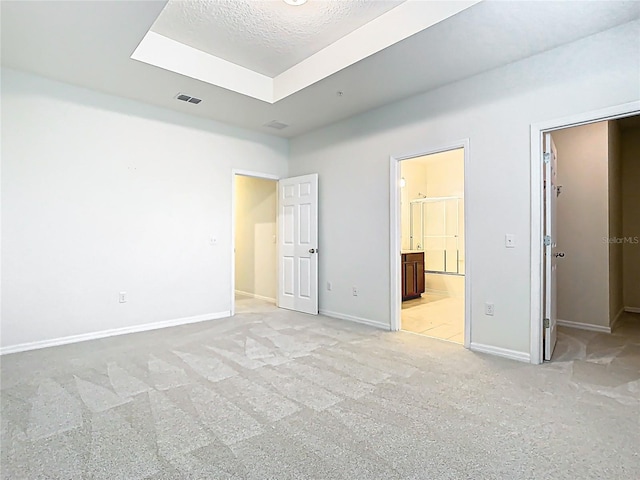 unfurnished bedroom featuring a walk in closet, a tray ceiling, light colored carpet, visible vents, and baseboards