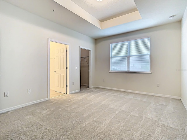 unfurnished bedroom featuring carpet floors, baseboards, a tray ceiling, and a walk in closet