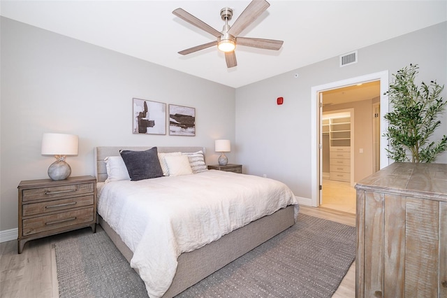 bedroom with a spacious closet, a closet, ceiling fan, and light hardwood / wood-style floors