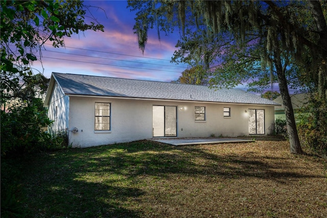 1073 Humphrey Blvd, Deltona, FL 32738 - back of house at dusk with stucco siding, a yard, a shingled roof, and a patio area
