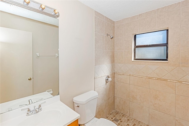 bathroom featuring a tile shower, vanity, a textured ceiling, and toilet