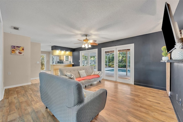 living room featuring ceiling fan, french doors, light hardwood / wood-style floors, and a textured ceiling