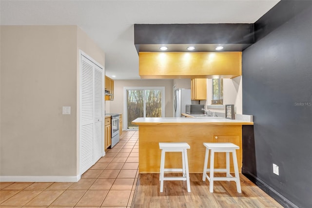 kitchen with kitchen peninsula, white fridge, stainless steel range with electric cooktop, and a breakfast bar area