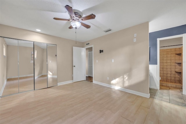 unfurnished bedroom featuring ensuite bathroom, ceiling fan, a textured ceiling, light hardwood / wood-style floors, and a closet