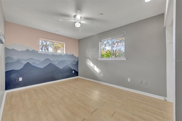 spare room featuring a textured ceiling, light wood-type flooring, ceiling fan, and a healthy amount of sunlight