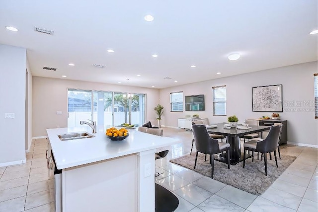 kitchen with light tile patterned floors, sink, and a kitchen island with sink