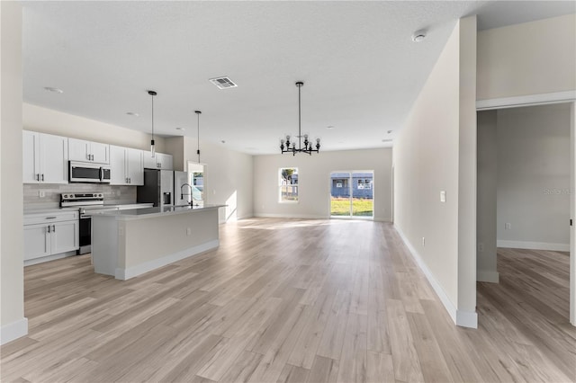 kitchen featuring white cabinets, an island with sink, appliances with stainless steel finishes, decorative light fixtures, and light hardwood / wood-style floors