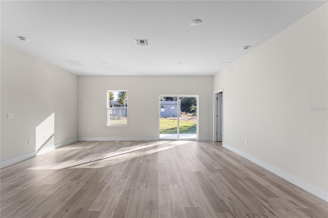 empty room with a textured ceiling and light hardwood / wood-style flooring